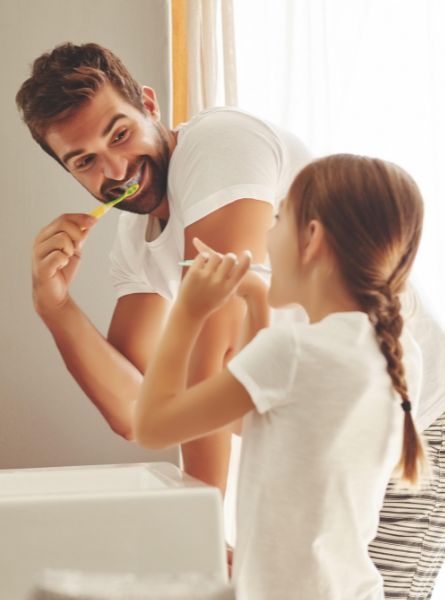 Mann und Mädchen putzen an einem Waschbecken Zähne.